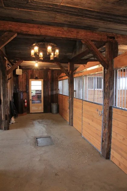 Allée d’écurie rustique avec box pour chevaux en bois et barreaux galvanisés Equinad.